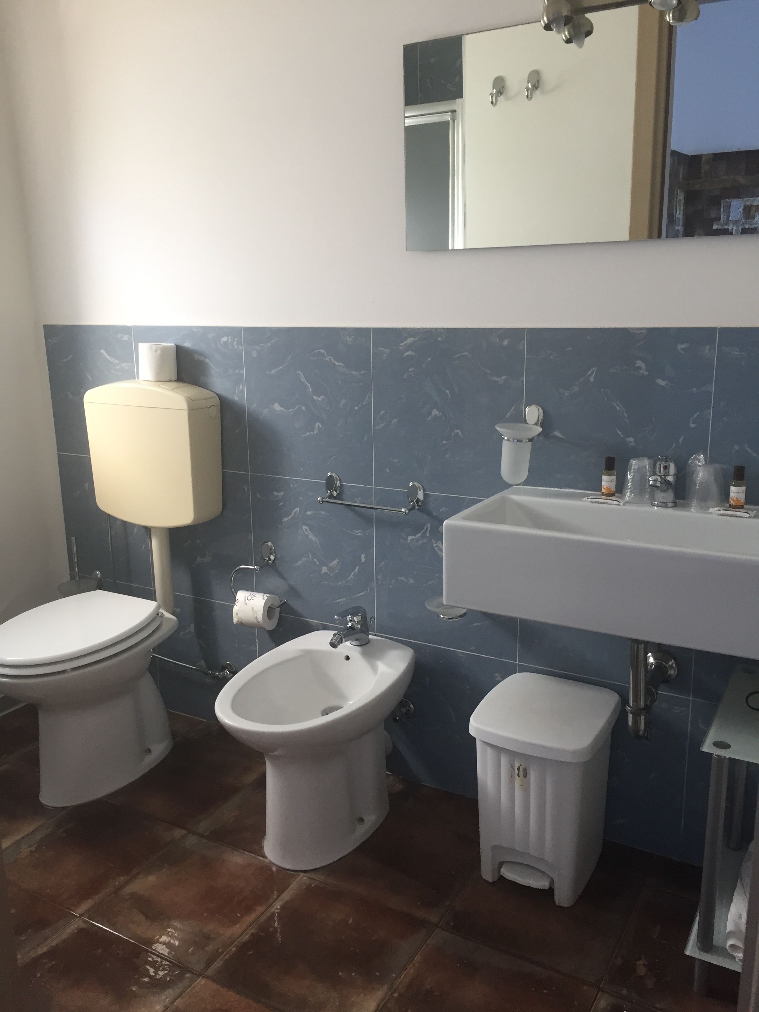 A bathroom with a toilet, bidet, sink, and a small trash bin.