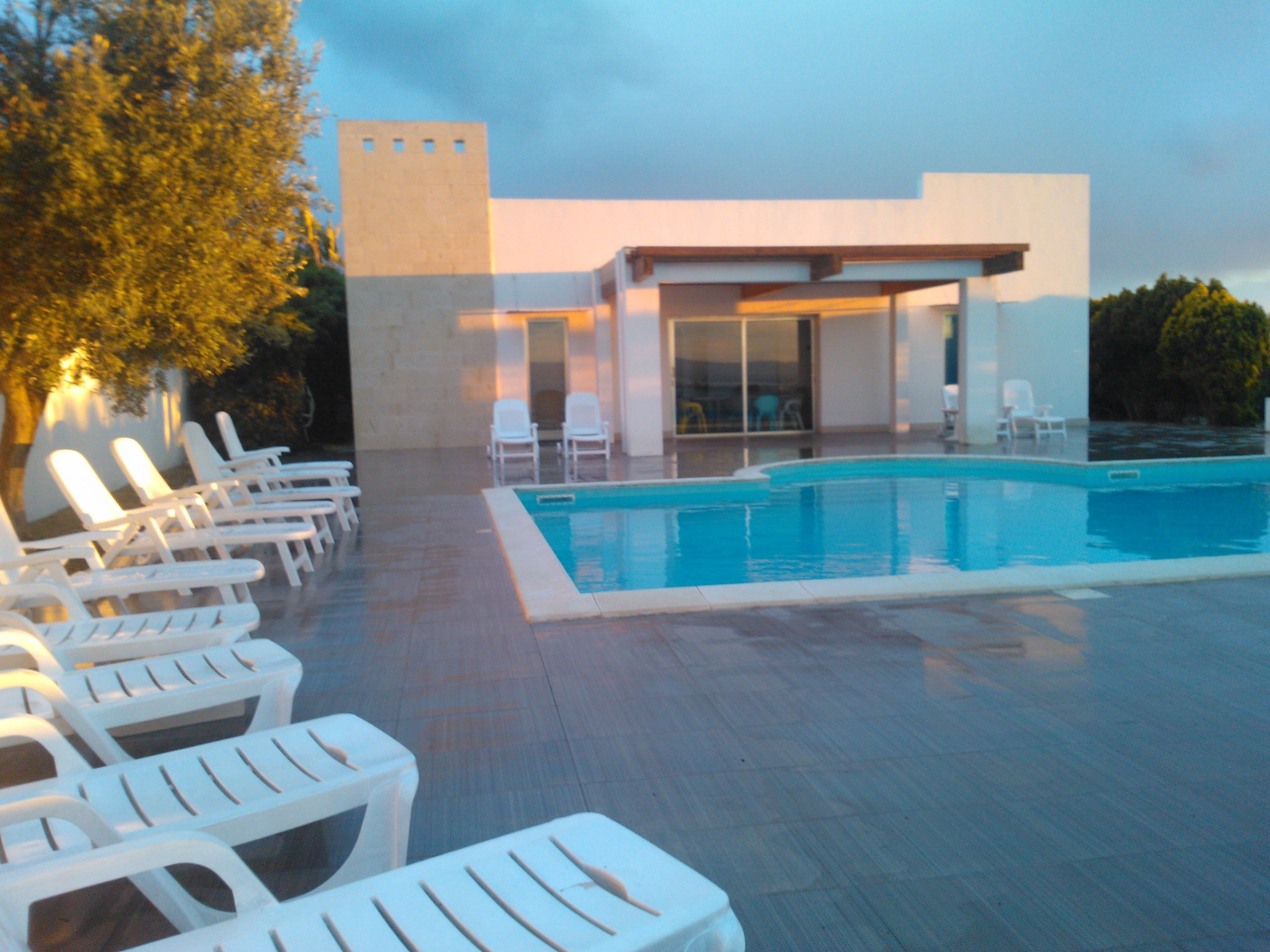Un área de piscina moderna con sillones de descanso y un edificio con grandes ventanales.