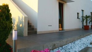 A modern building with a sloped roof, a staircase leading to an entrance, and a pathway with white pebbles. - B&B Resort Torrefano (Pachino)