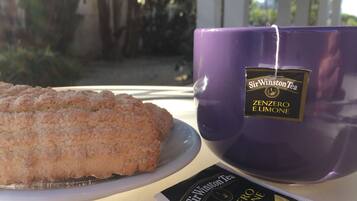 Una bustina di tè Sir Winston Tea Zenzero e Limone viola, un piatto con una pasticceria e una confezione di tè su un tavolo.