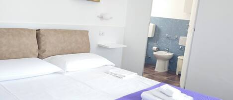 A hotel room with a large bed, a bathroom visible through an open door, and artwork on the walls.