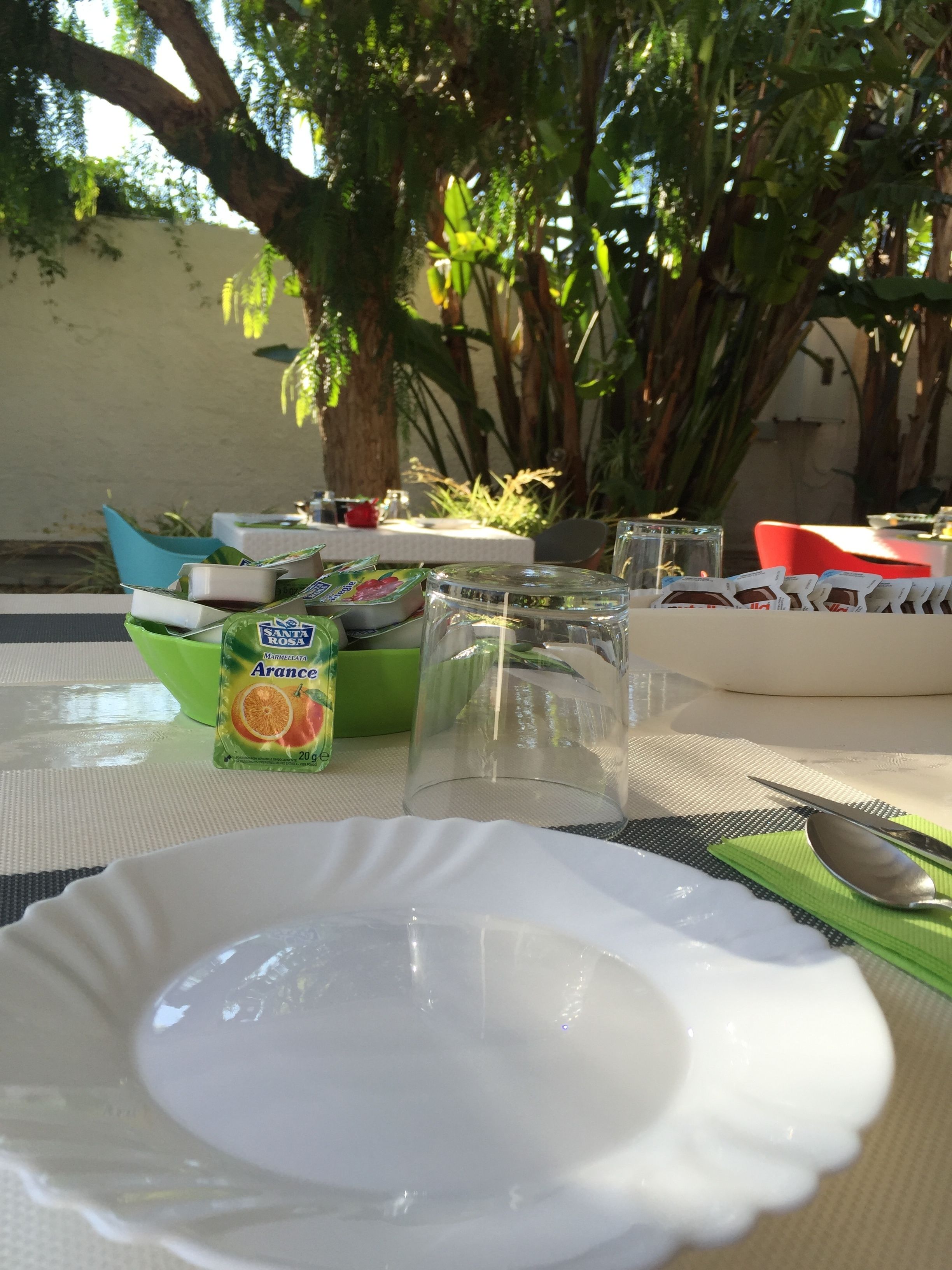 A dining table with a white plate, a glass container, and a packet of orange marmalade.