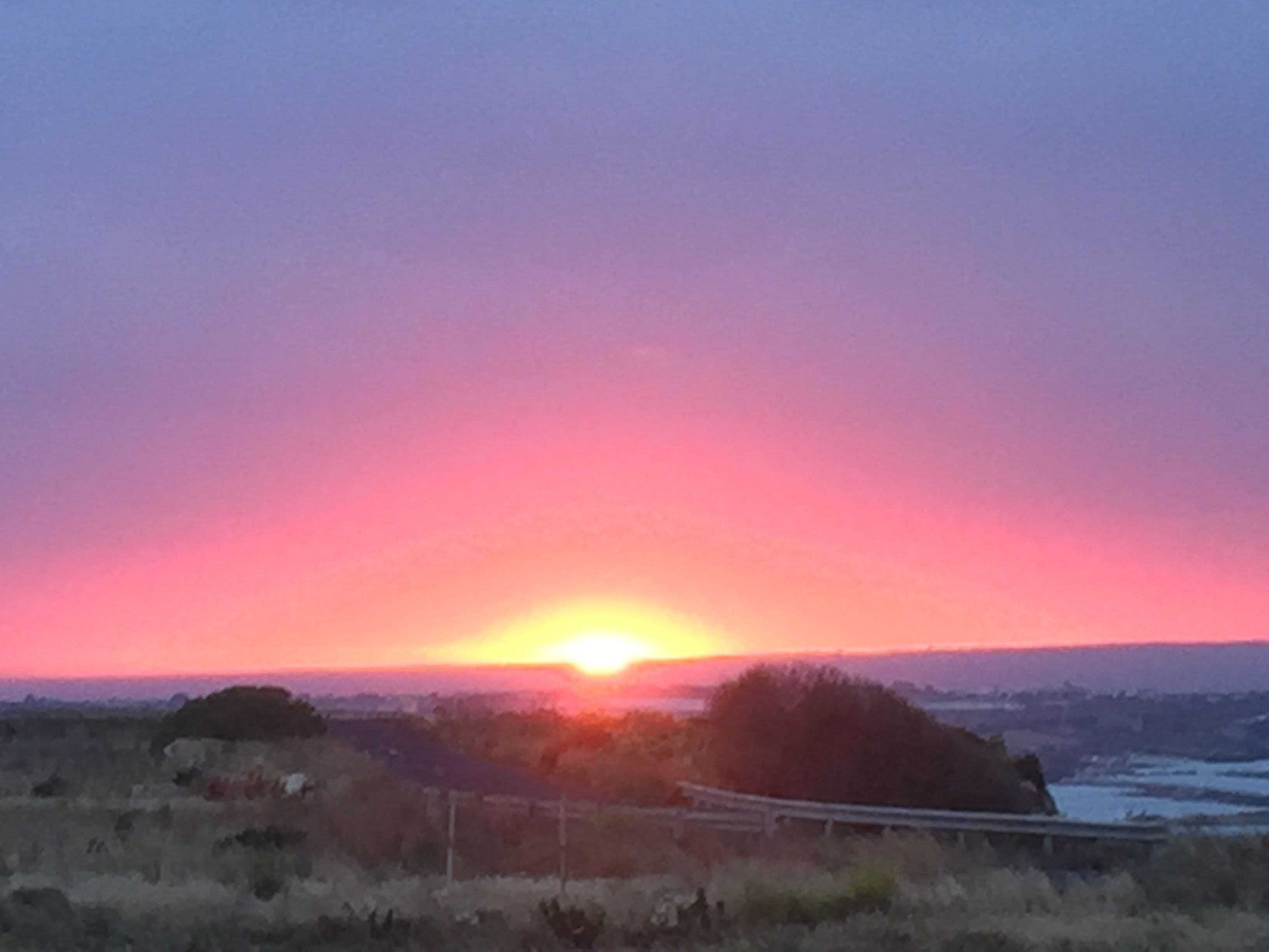 Un coucher de soleil sur un paysage comprenant un pont et des collines lointaines.