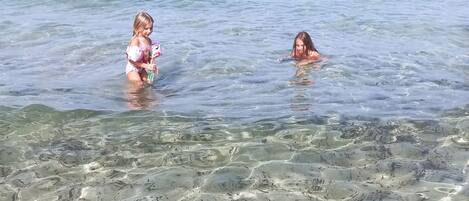 Escena de playa con aguas claras y poco profundas, gente nadando y jugando.