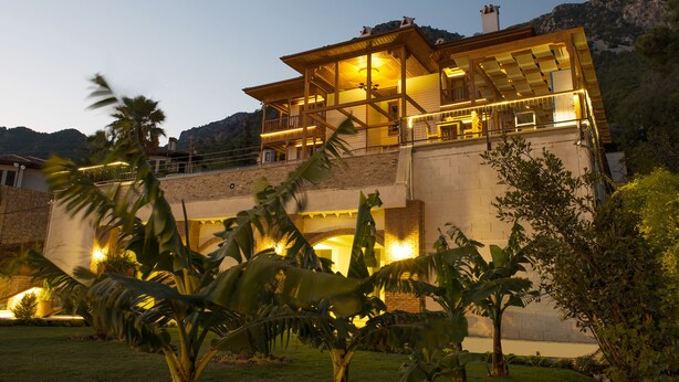 Una casa de dos pisos con balcón, rodeada de plantas tropicales.