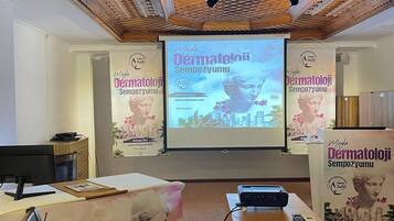 Un salón de conferencias con techo de madera, una pantalla para proyector y carteles para un evento.