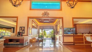 Un hall de hotel con mostrador de recepción, zona de estar y una gran pantalla de televisión.