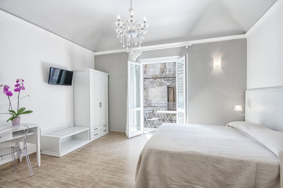 A bedroom with a bed, a desk, a chair, a TV, and a balcony.