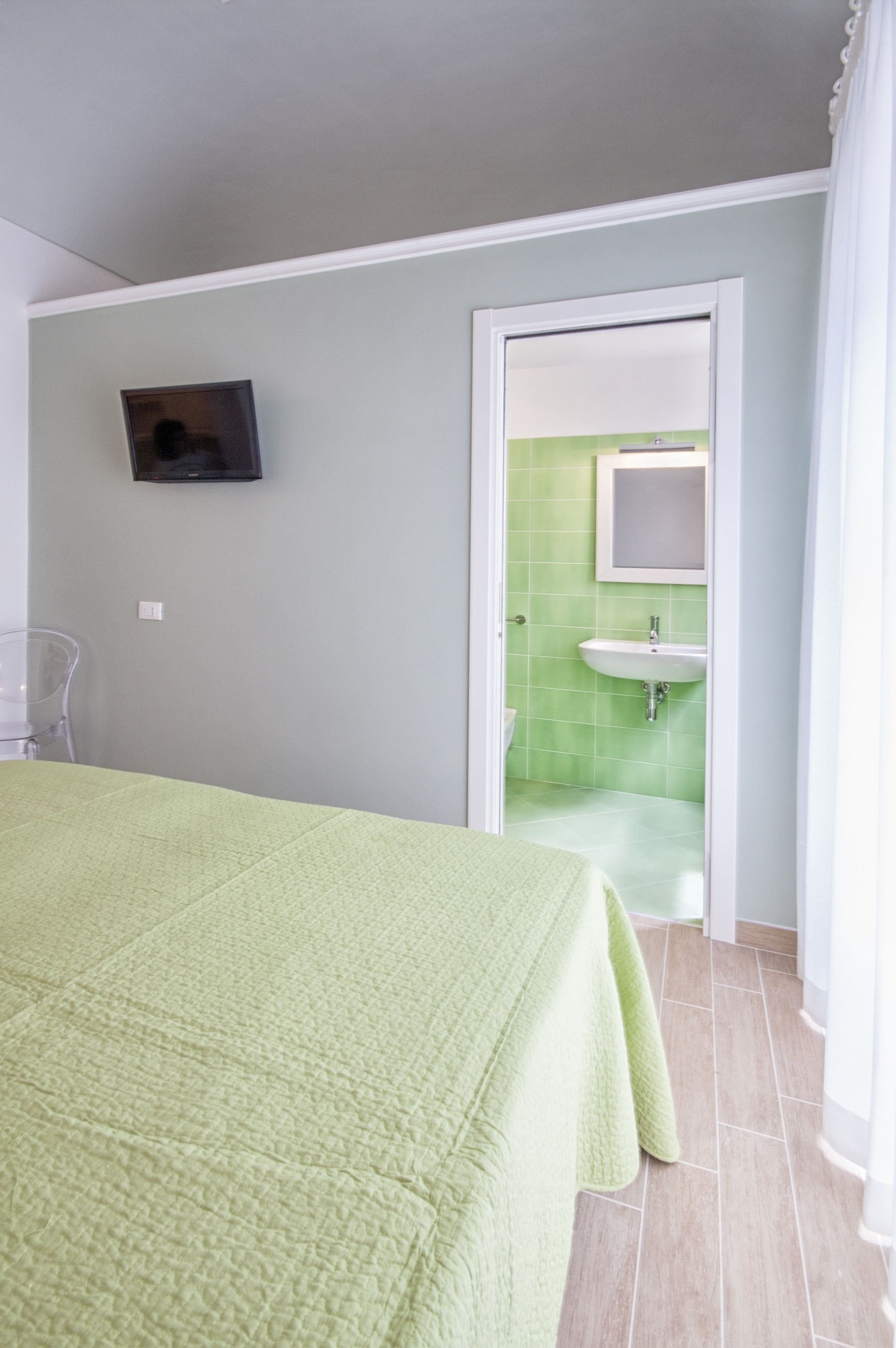 Een kamer met een bed, een aan de muur bevestigde televisie en een badkamer zichtbaar door een open deur.