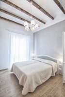 Un dormitorio con cama, vigas de madera, una araña y una ventana con cortinas.