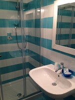 Un baño con ducha de vidrio, un lavamanos blanco y un espejo encima.