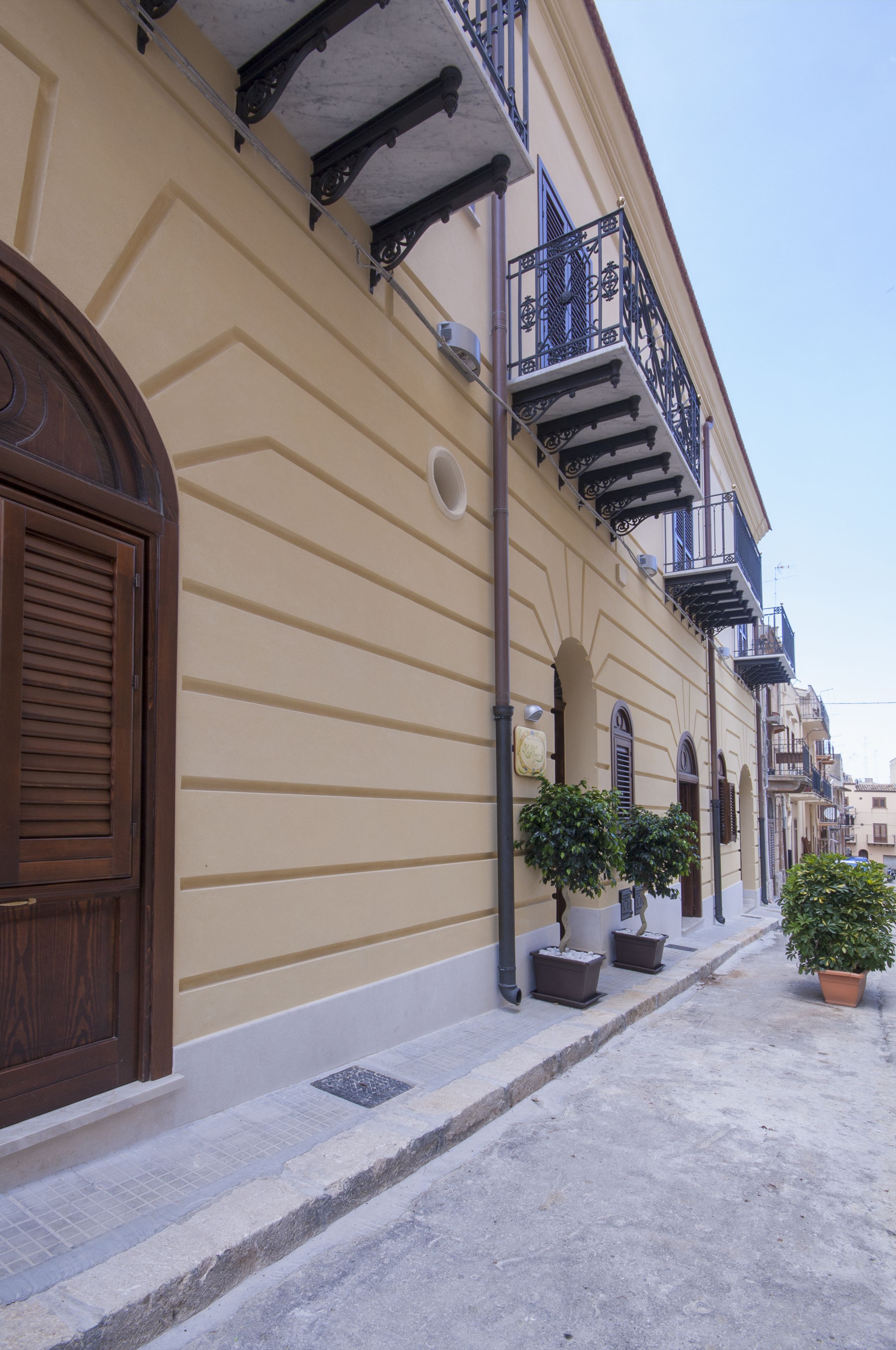 A building with a beige facade, wooden shutters, and a tiled sidewalk.