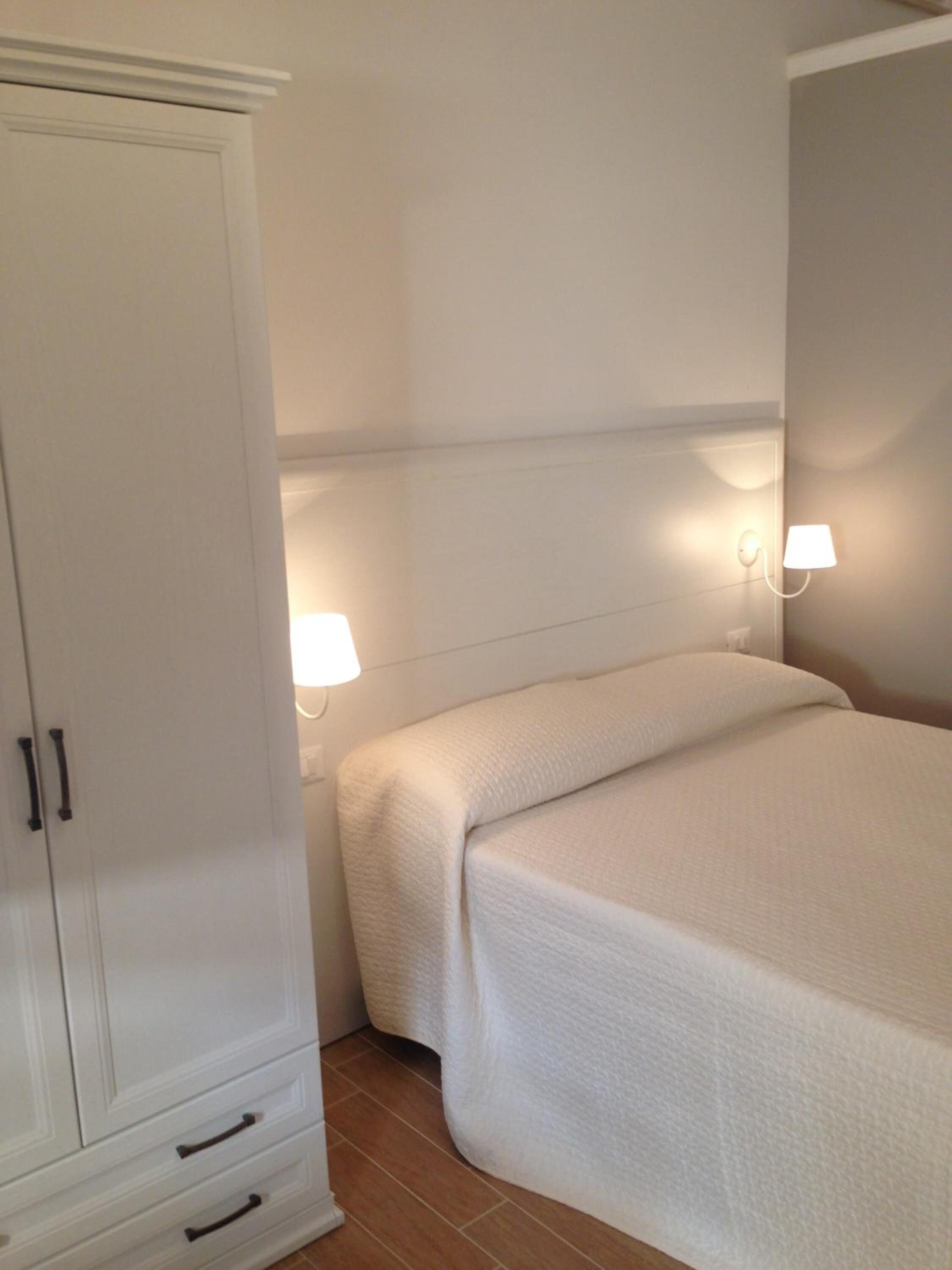 A bedroom with a bed, a wardrobe, and two wall-mounted lamps.