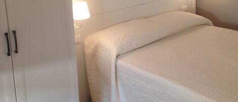 A bedroom with a bed, a wardrobe, and two wall-mounted lamps.