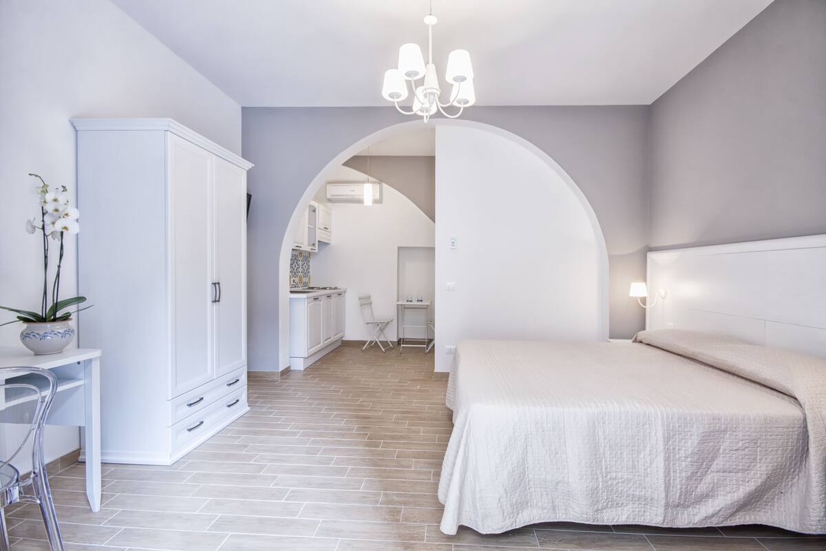 A modern bedroom with a large bed, a desk, and a wardrobe.