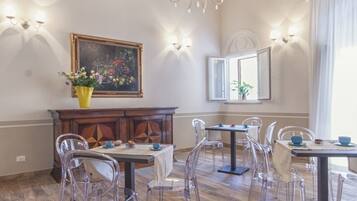 A dining area with wooden flooring, clear chairs, a chandelier, and a painting on the wall.