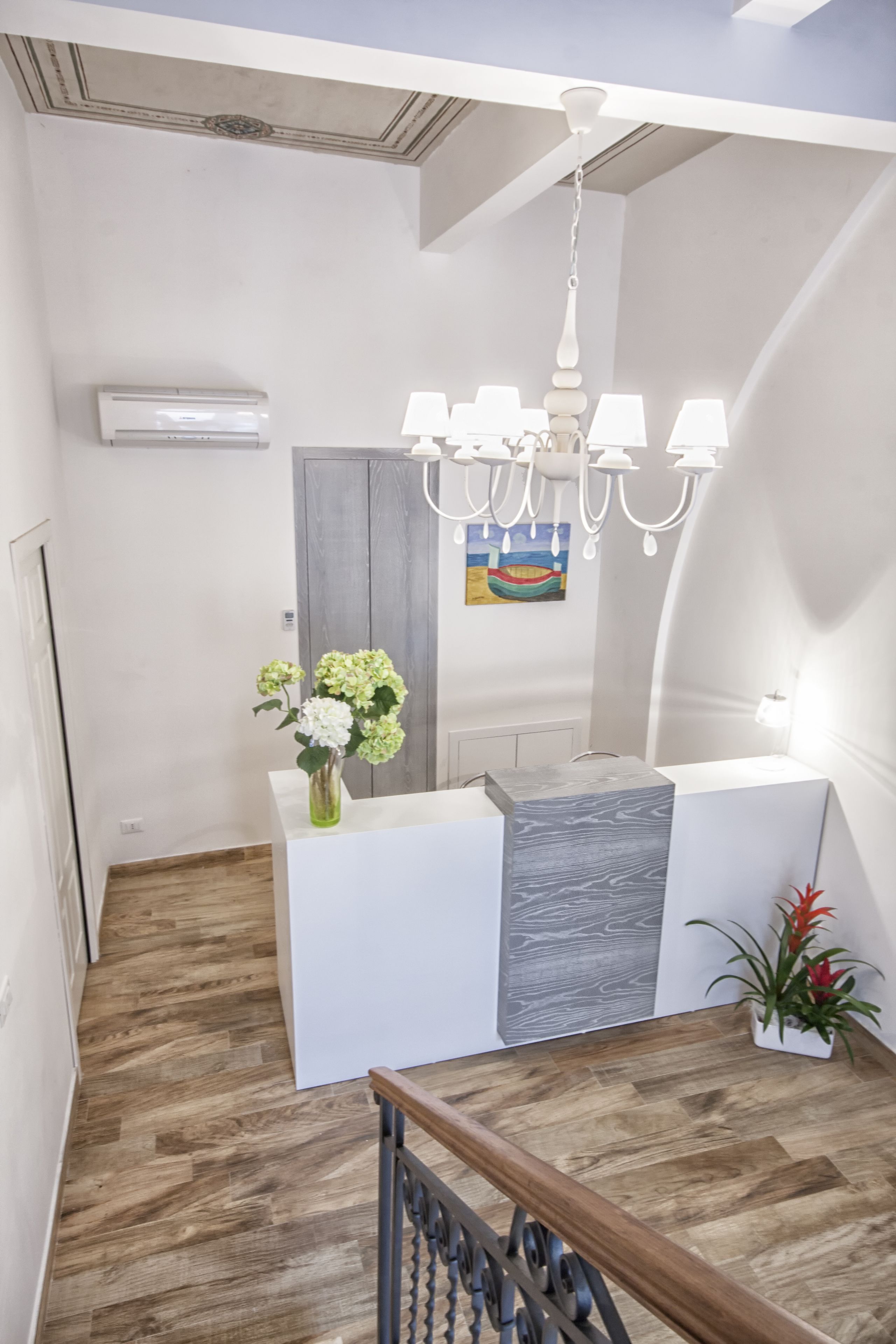 Una zona de recepción moderna con suelo de madera, un mostrador blanco, una pared de acento gris, una araña y un cuadro en la pared.