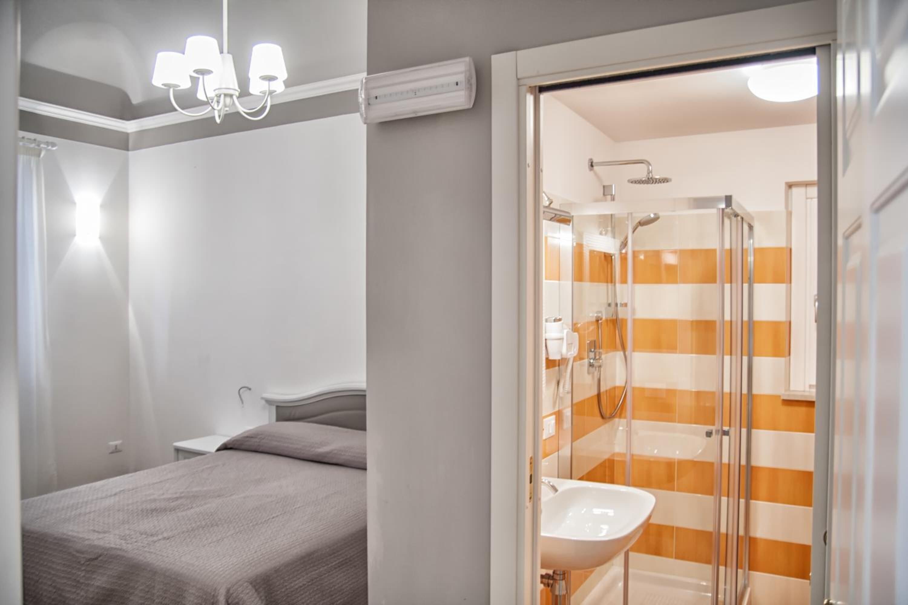 A hotel room with a bed, a bedside table, a shower with a glass door, and a bathroom with a sink.