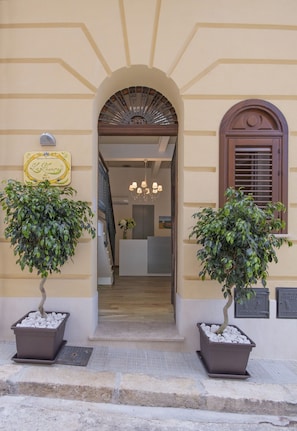 An entrance with a central archway, two potted trees, and a reception desk visible through the doorway. - Residenza Le Zagare (Castellammare del Golfo)