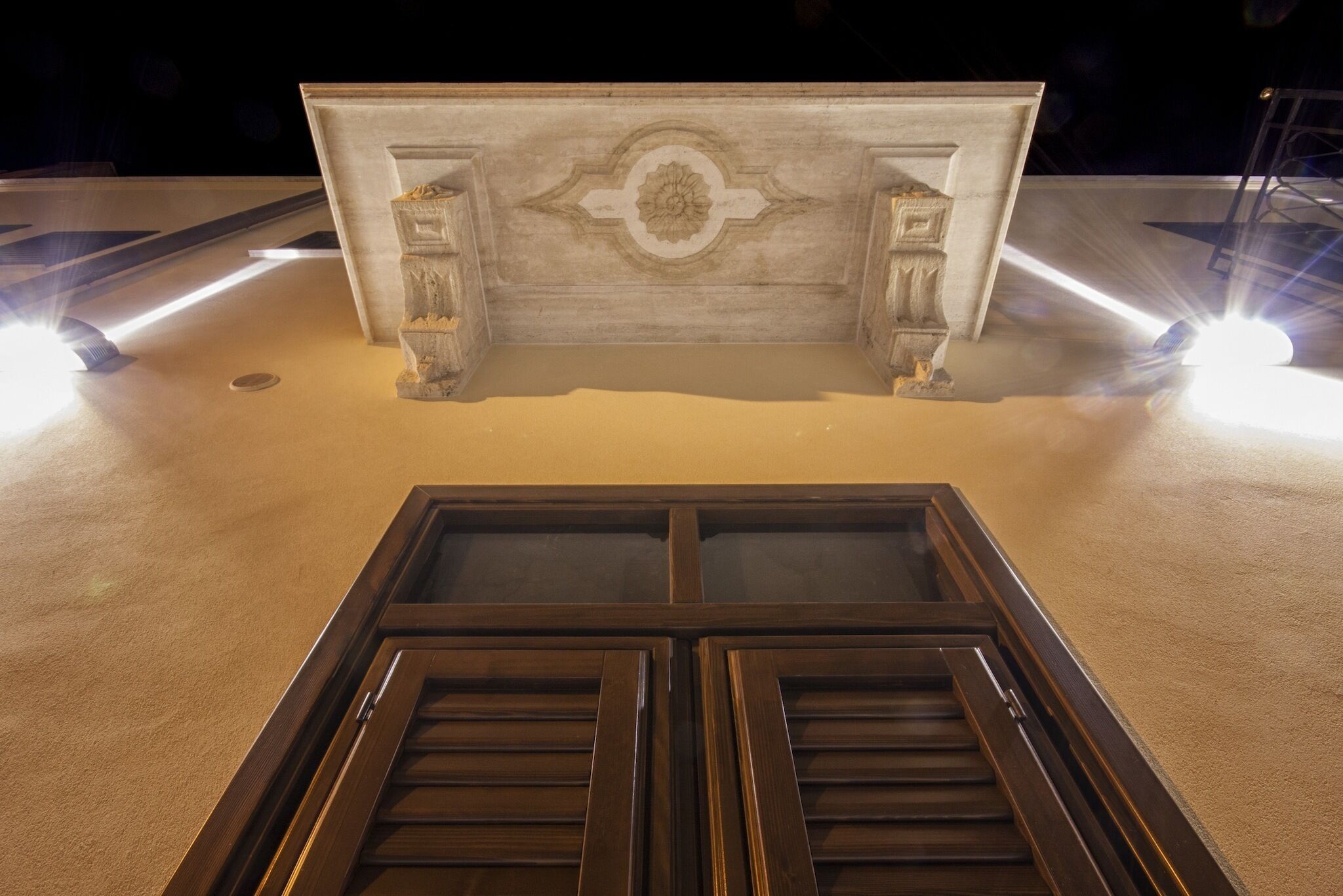 A marble reception desk with a central decorative panel and two columns, flanked by two large, dark wooden doors.