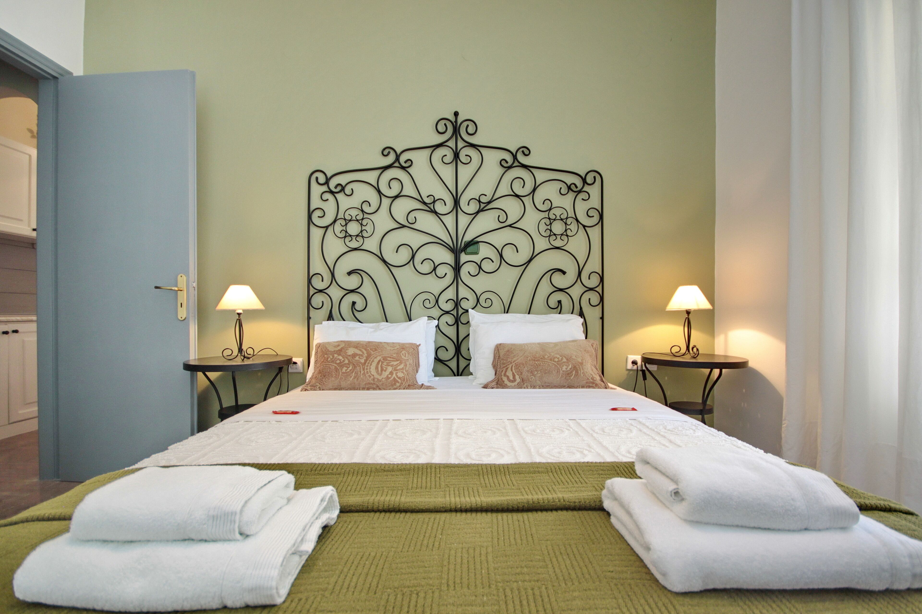 Una cama bien hecha con un cabecero decorativo, dos lámparas de noche y una manta verde.
