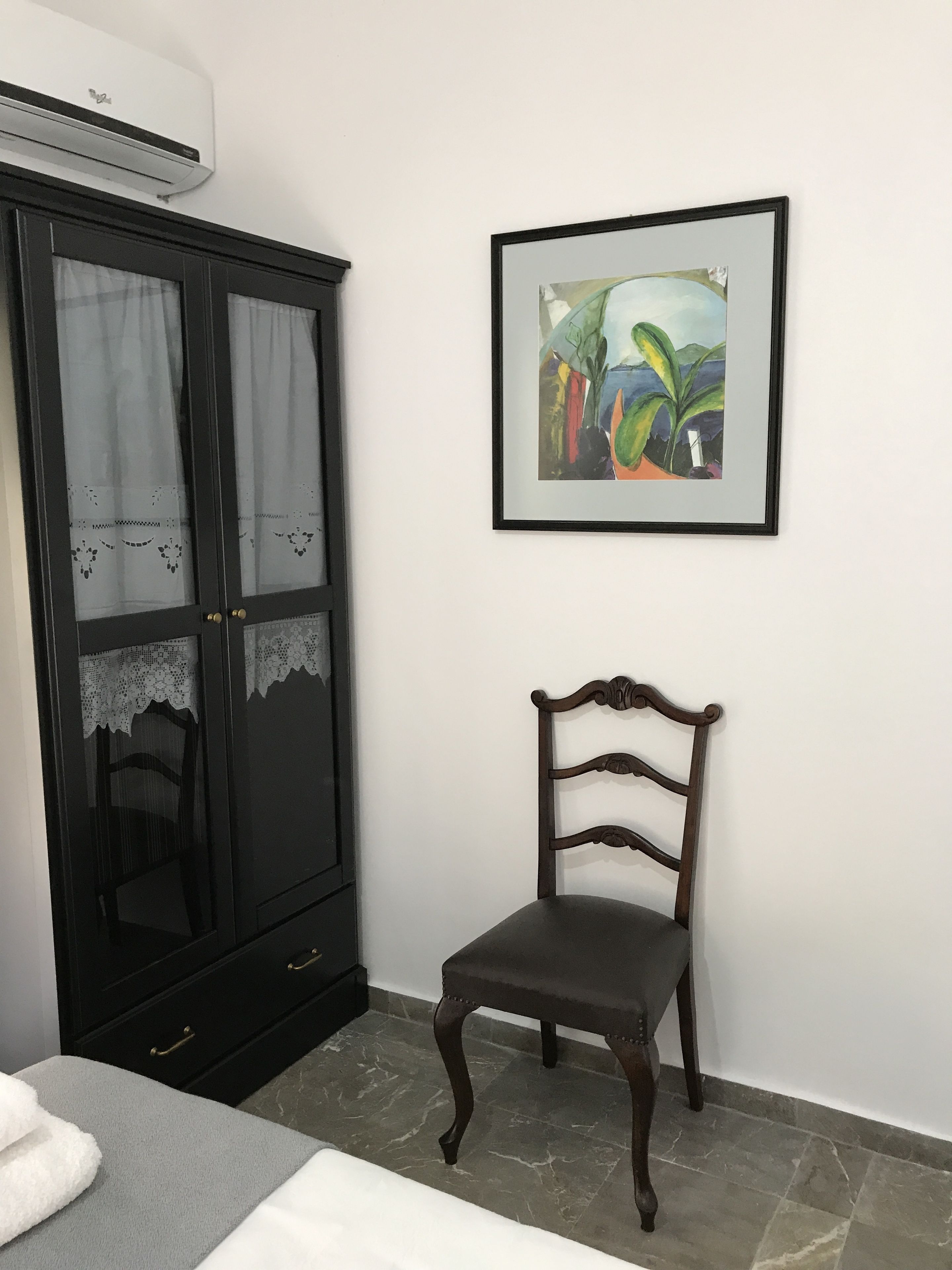 Une pièce avec une armoire noire, un tableau abstrait encadré et une chaise en bois.