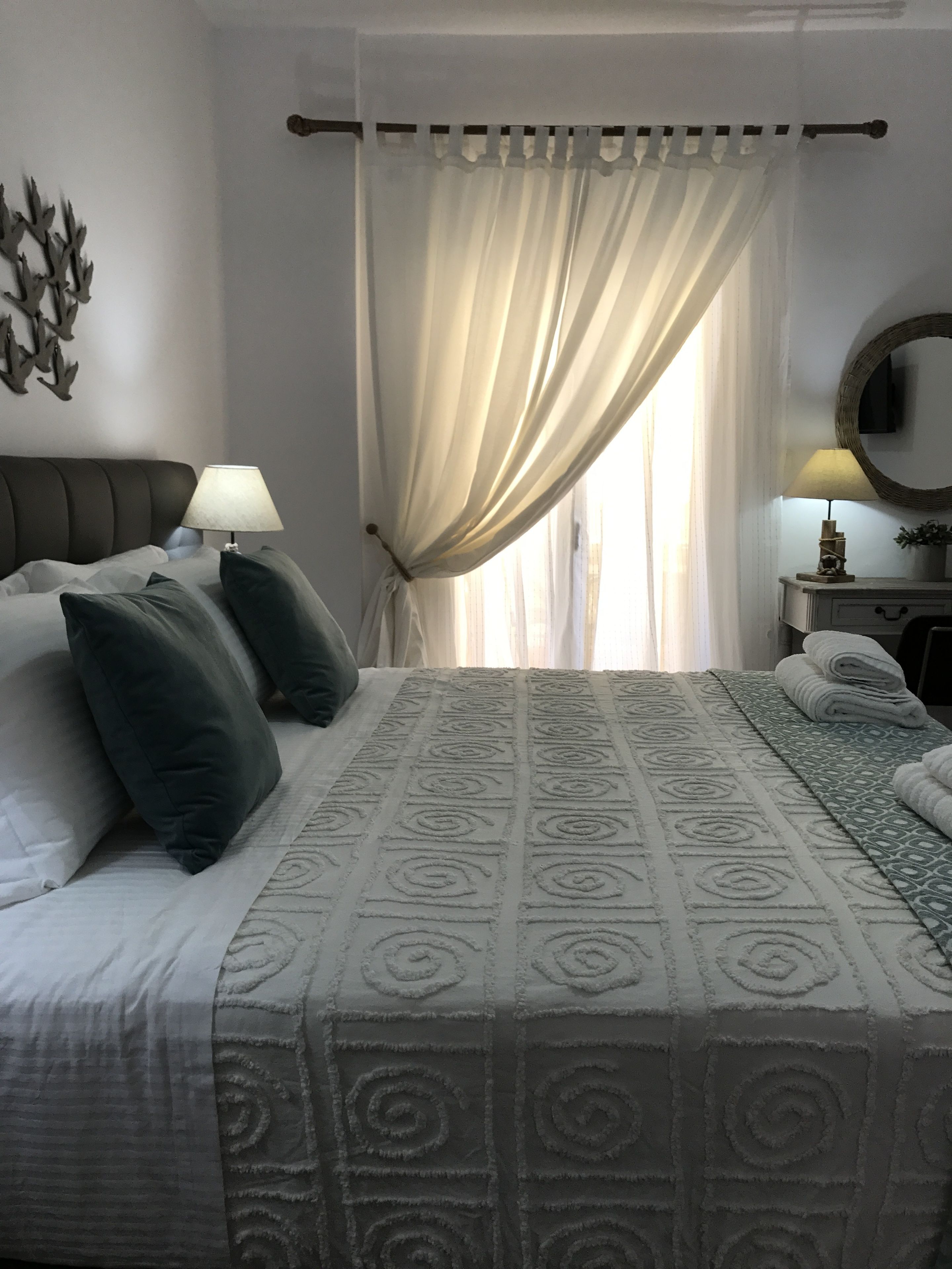 A neatly made bed with a patterned bedspread, a bedside lamp, and a wall-mounted mirror.