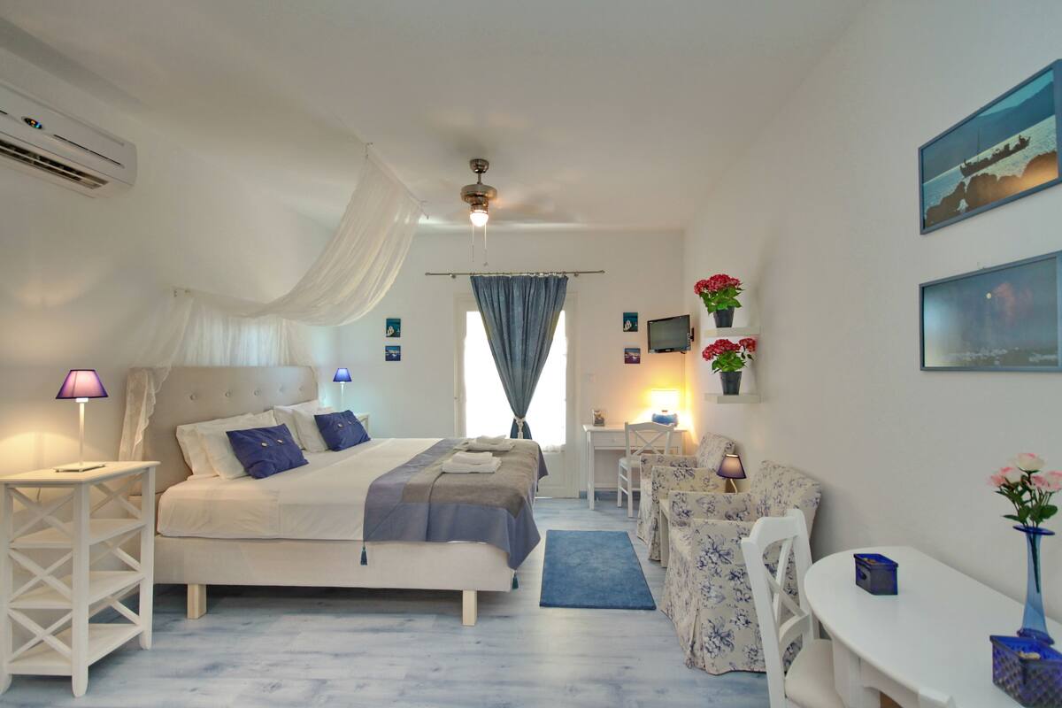 A bedroom with a bed, bedside tables, a desk, a chair, and a small table with a vase of flowers.