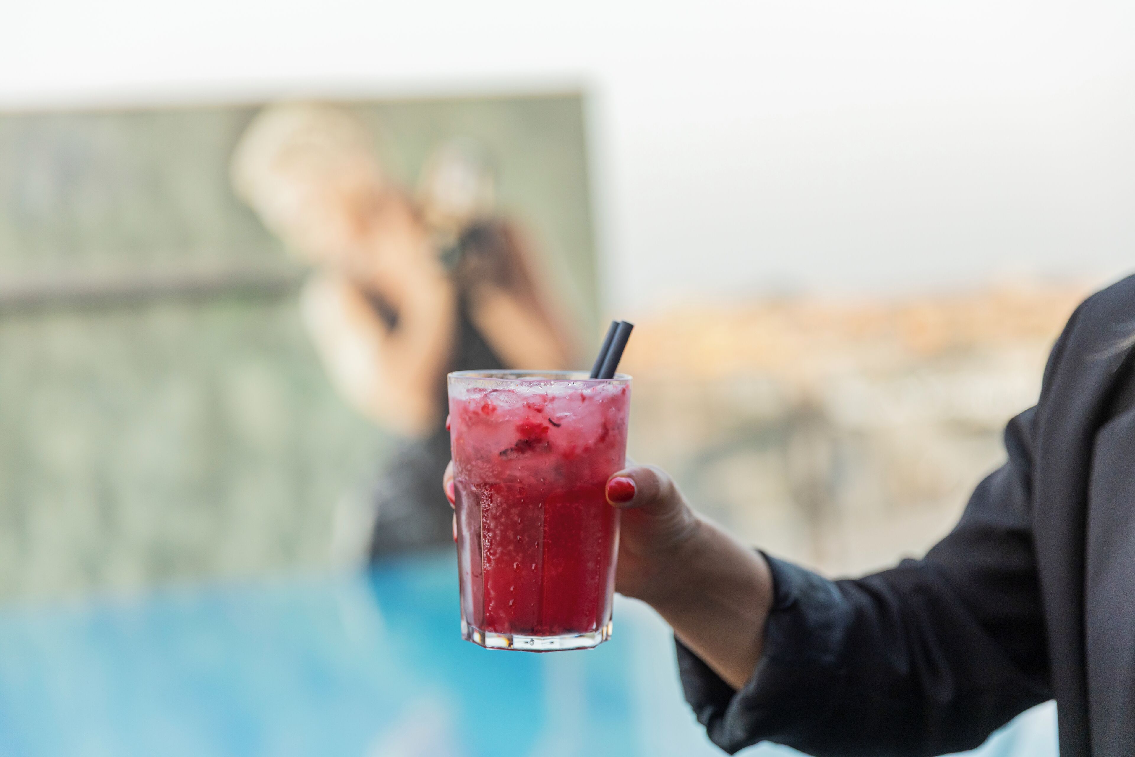 A person holding a glass with a straw, with a blurred background.