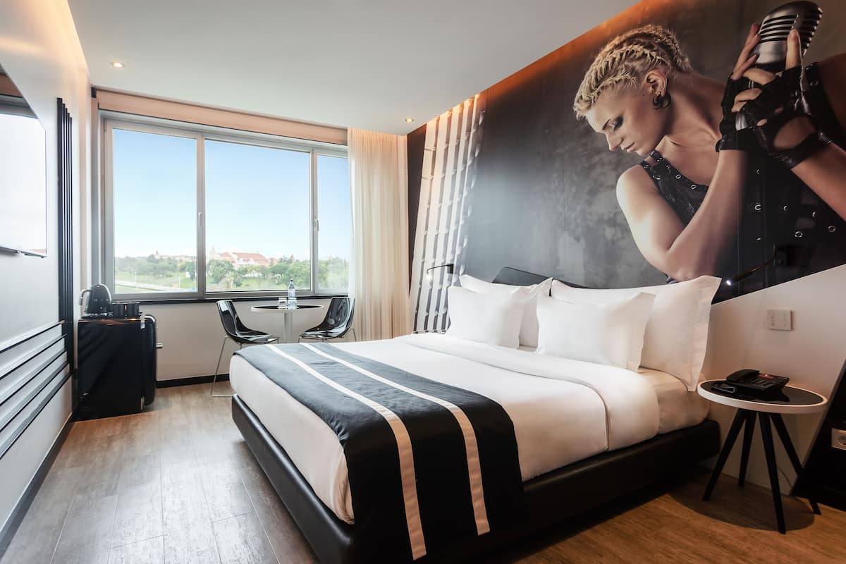 A modern hotel room with a large bed, a desk, and a view of the city.
