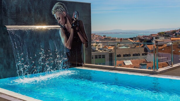 Una piscina con caída de agua, vista panorámica de la ciudad y una persona sosteniendo un micrófono.