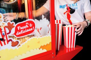 A popcorn machine with a sign that reads "Fresh & delicious!" and a person wearing a white shirt with "FENTIX MUSIC" on it.