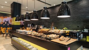 Zona de bufé con diversos alimentos, una cafetera y platos apilados en una barra.
