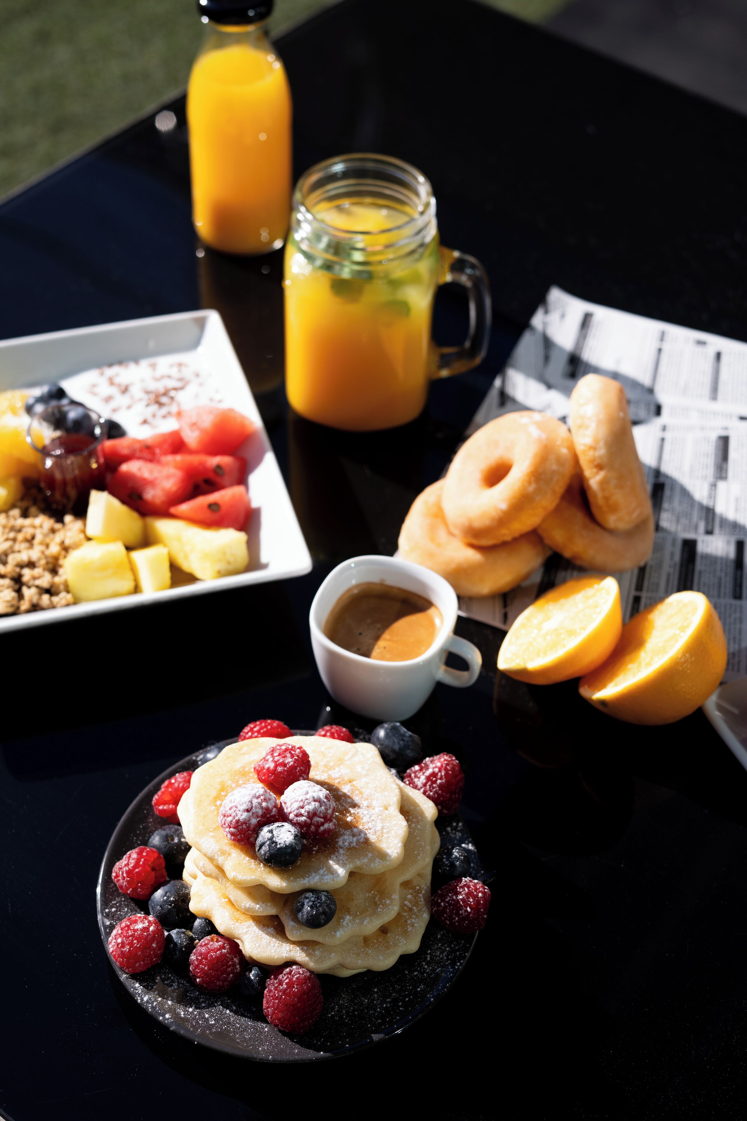 Uma mesa posta para o café da manhã, com panquecas, frutas vermelhas e suco de laranja.