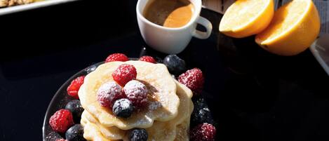Uma mesa posta para o café da manhã, com panquecas, frutas vermelhas e suco de laranja.