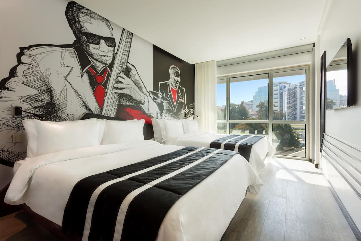 A hotel room with two beds, a large cityscape view, and a mural on the wall.