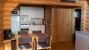 A cozy log cabin interior with a dining area, kitchen, and a TV mounted on the wall. - Karelia Country Cottages (Kitee)