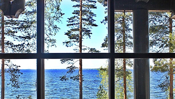 A view through a window with a wooden deck, a white lantern, and a clear blue sky. - Karelia Country Cottages (Kitee)