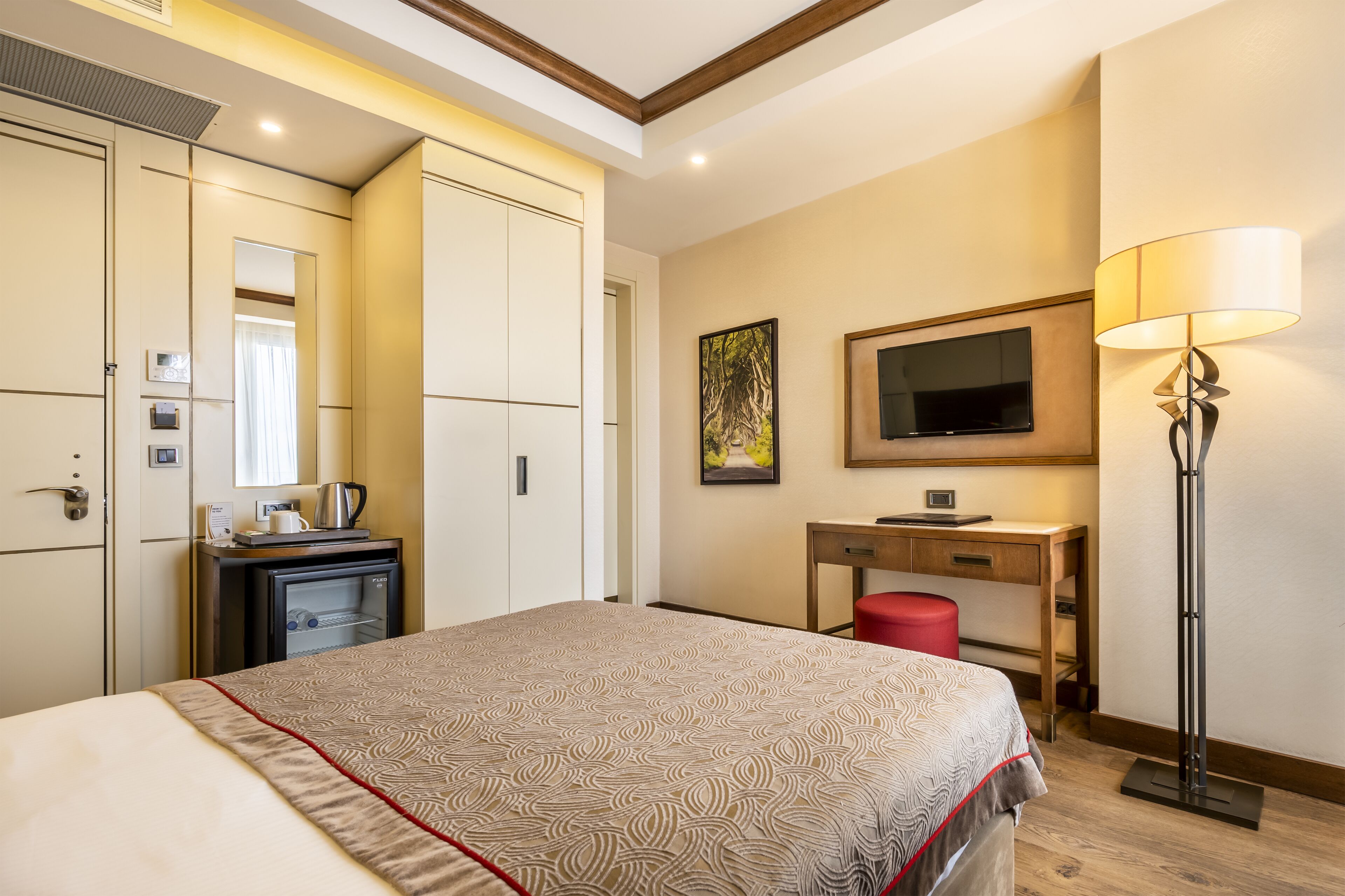 A hotel room with a bed, a desk, a TV, a lamp, and a wardrobe.