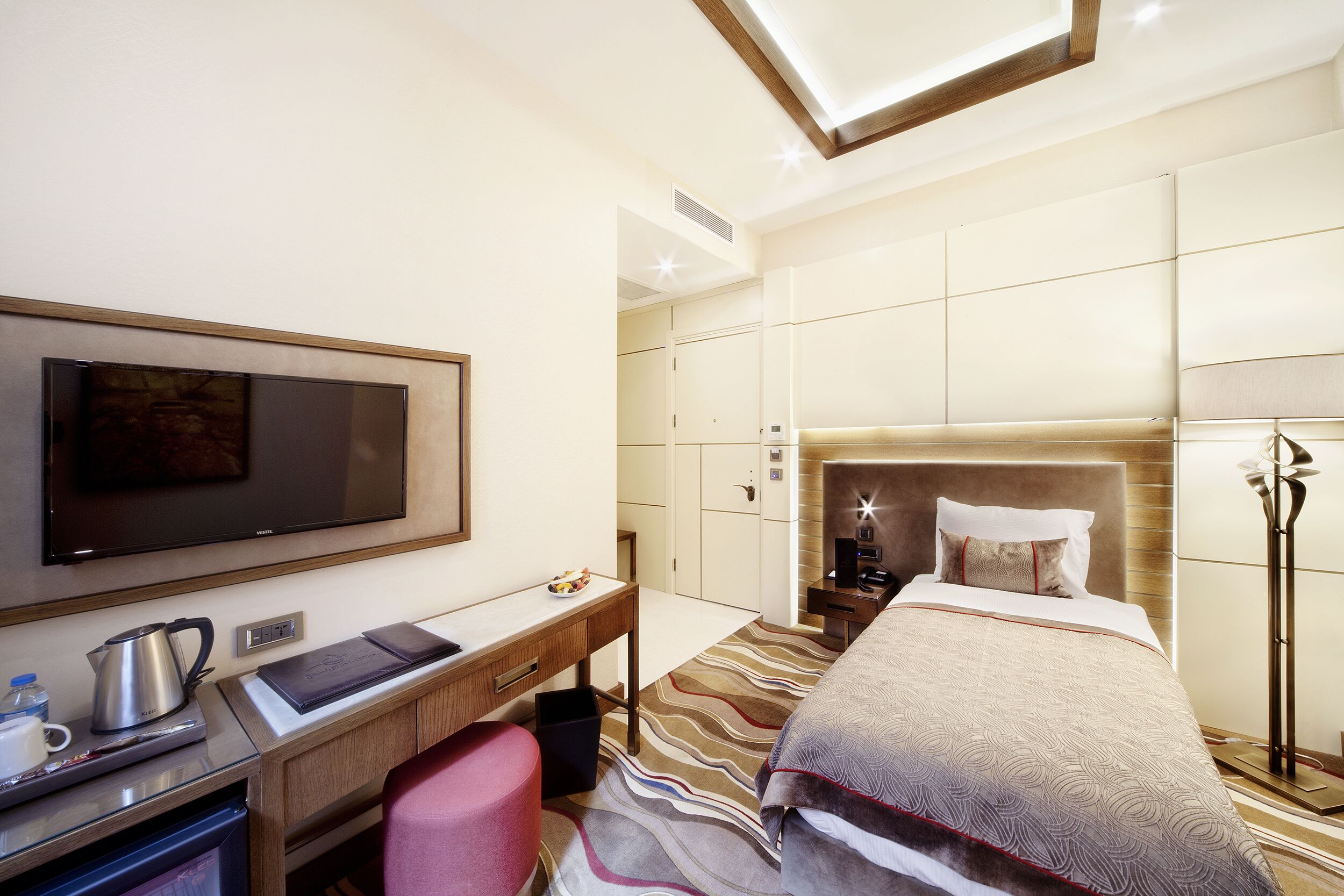 Habitación de hotel con cama, escritorio, televisor, cafetera y lámpara.