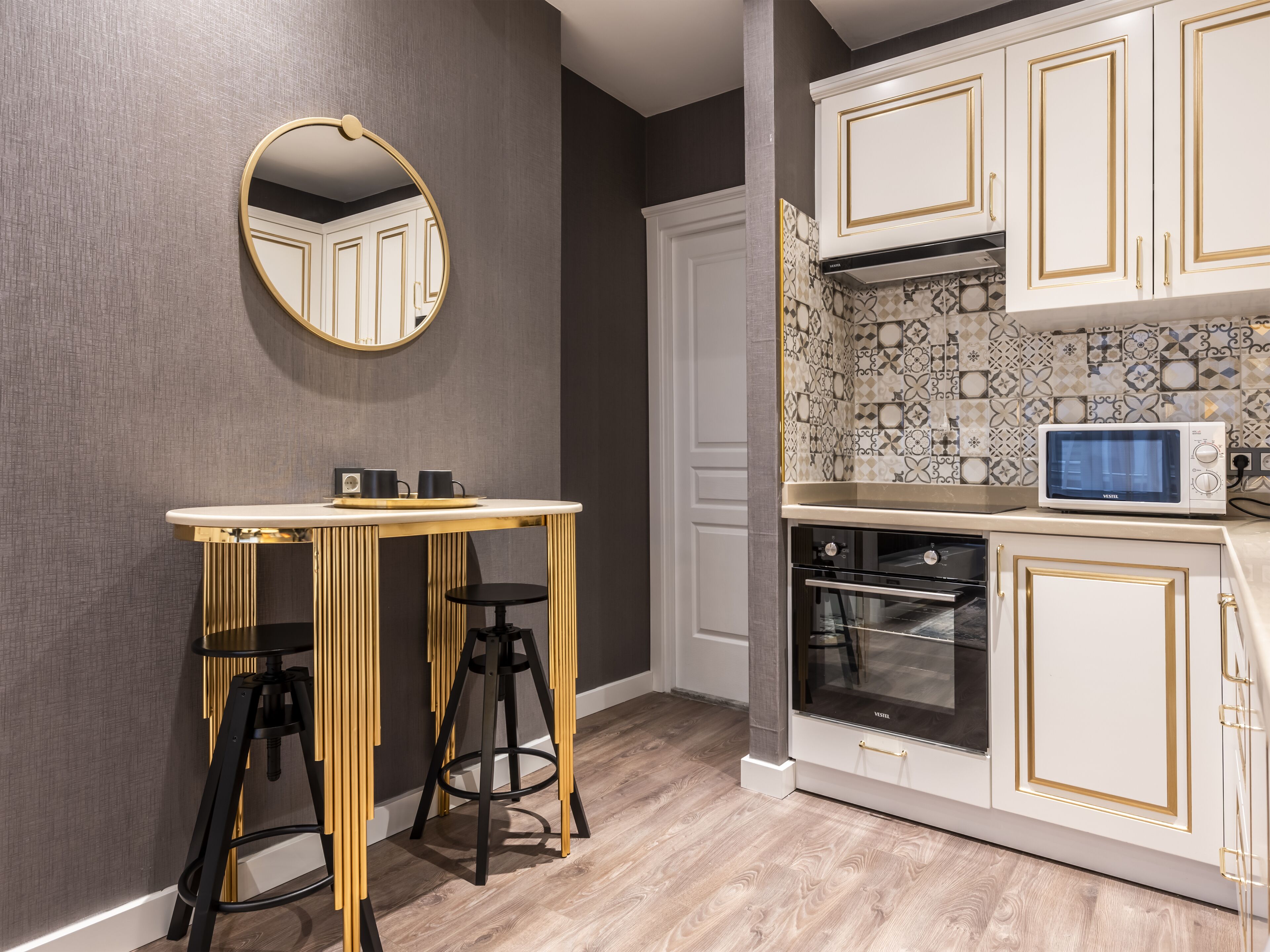 A modern kitchen with white cabinetry, a microwave, and a round mirror.