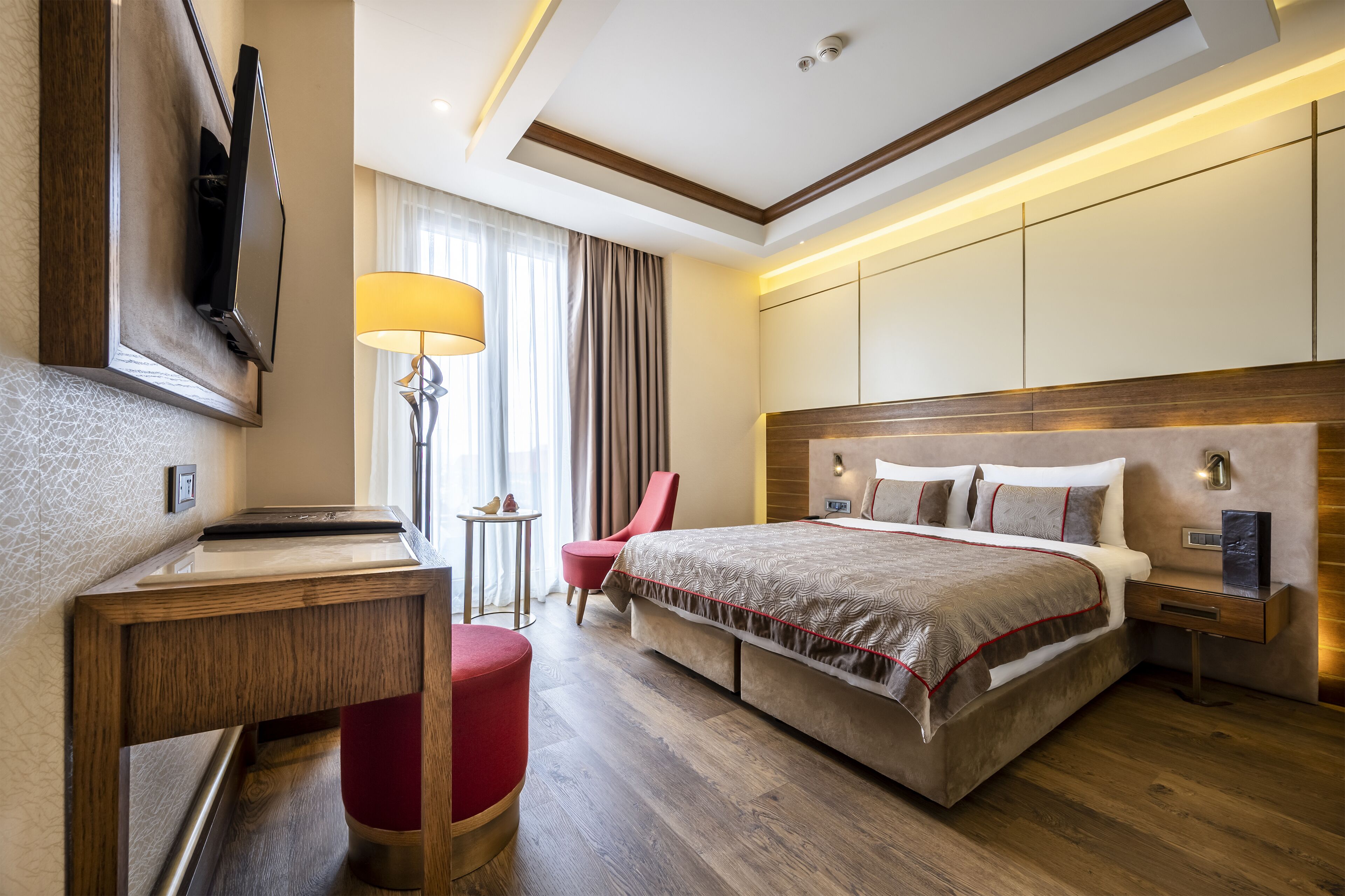 A modern hotel room with a large bed, a desk, a chair, and a TV mounted on the wall.