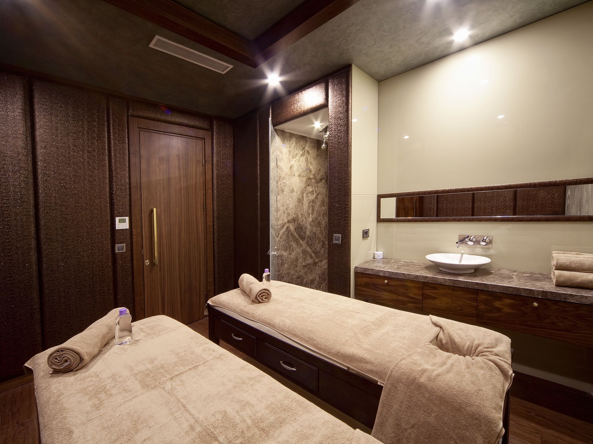 Quarto de hotel com duas camas, um espelho grande, pia e guarda-roupa de madeira.