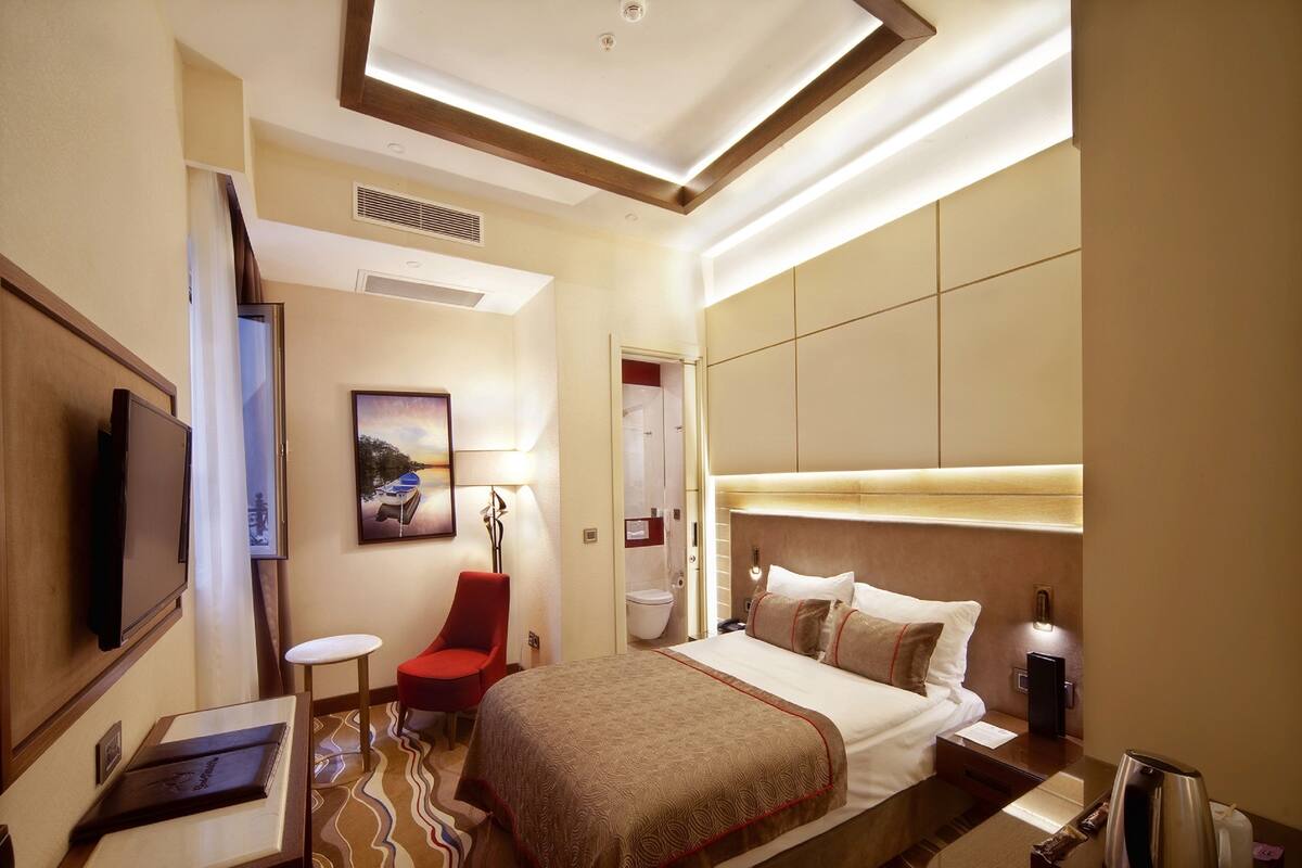 A hotel room with a bed, a TV, a desk, a chair, and a bathroom door.
