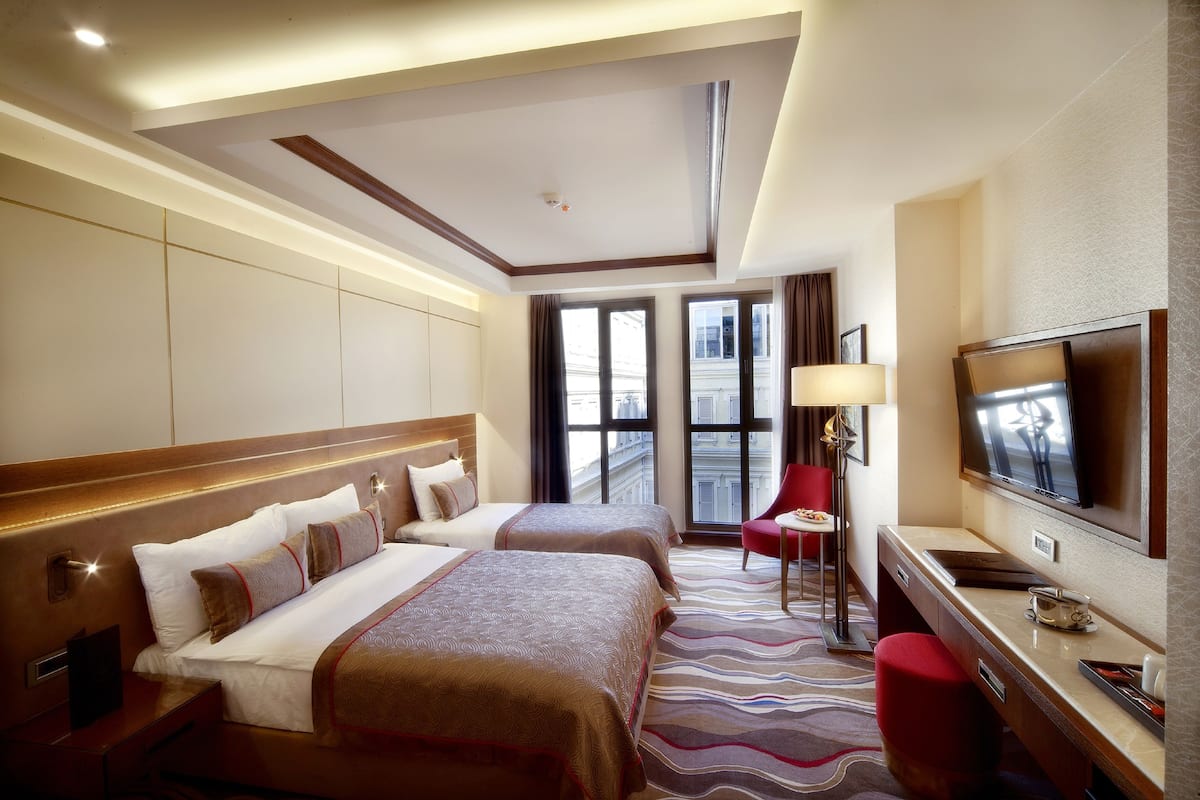 A hotel room with two beds, a TV, a desk, and a view of the city.