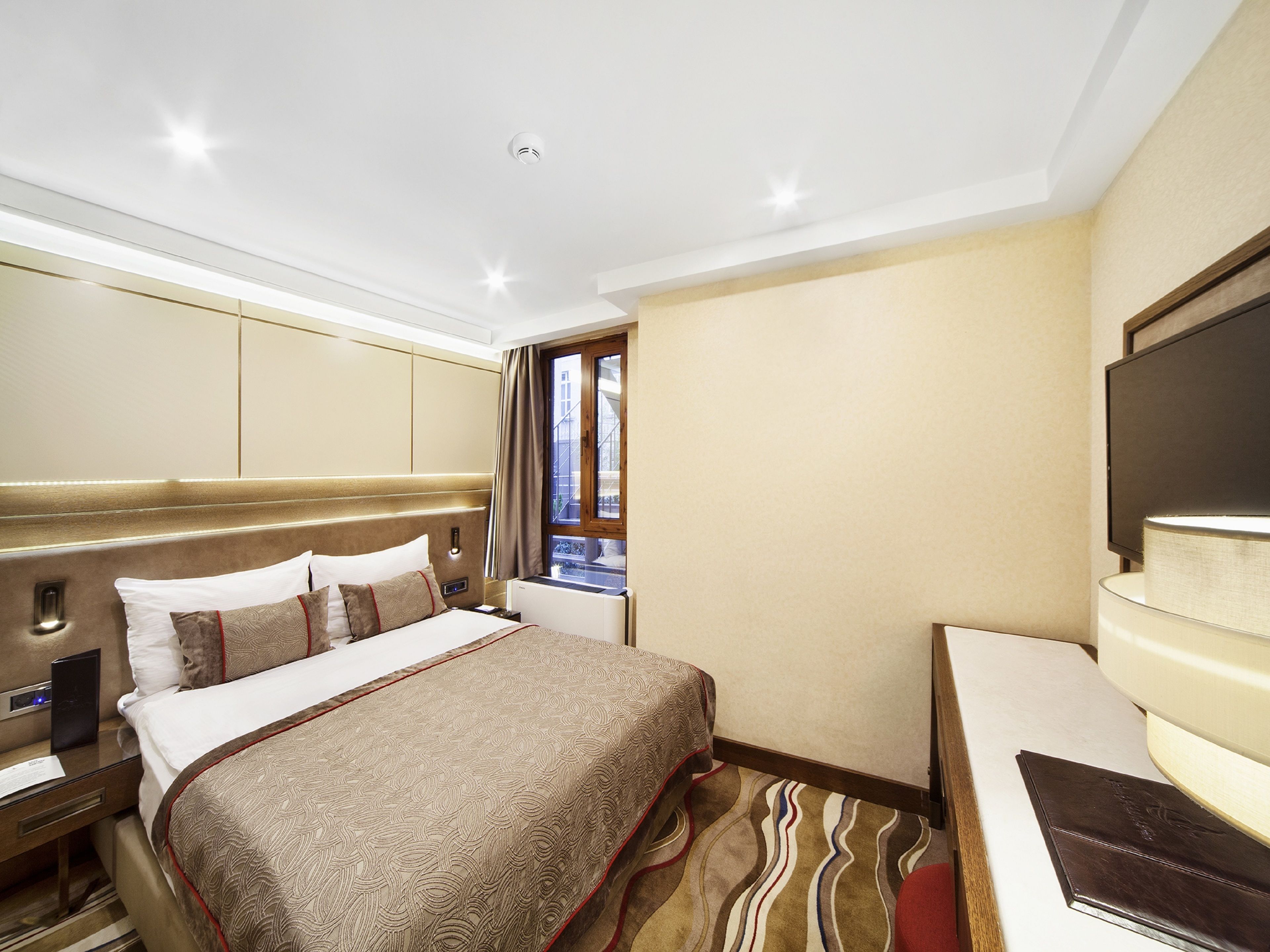 Habitación de hotel con una cama grande, escritorio, televisión de pantalla plana y ventana con vista a edificios.