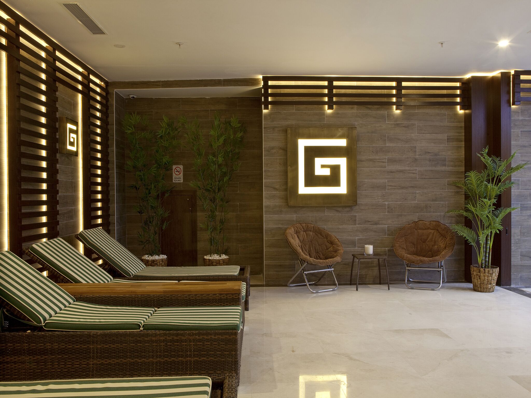 A modern lounge area with wicker lounge chairs, a wall-mounted light fixture, and a potted plant.