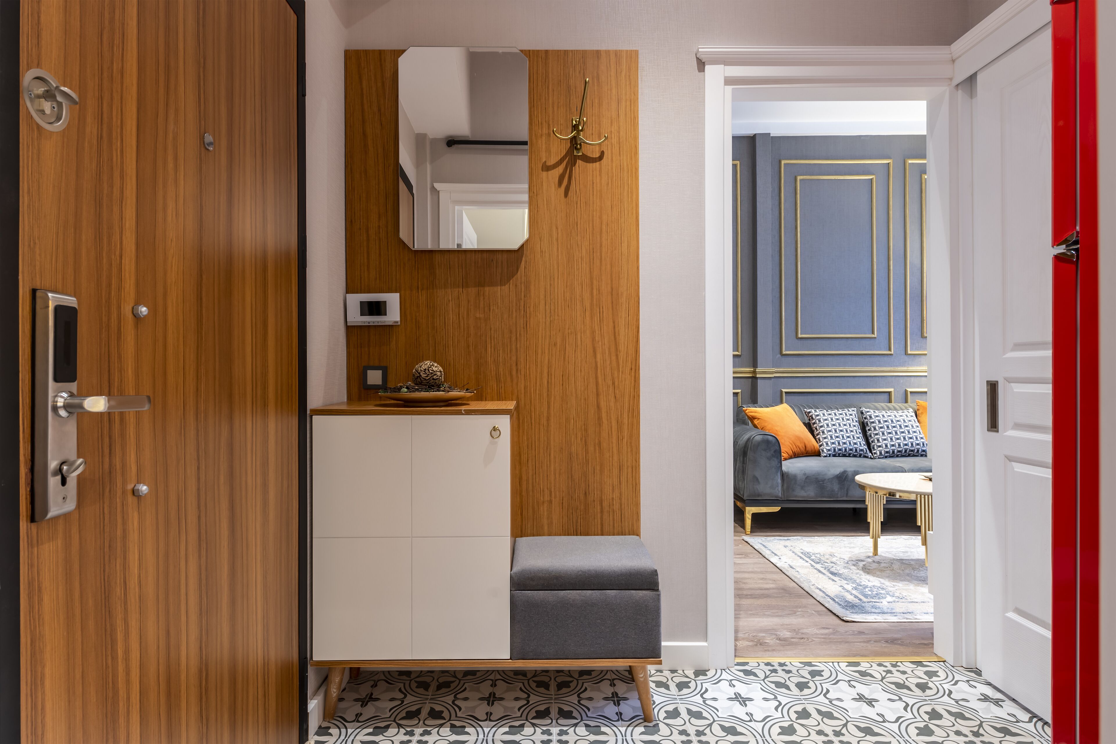 Una habitación moderna con un armario de madera, un mueble blanco, un banco gris, un espejo y una puerta roja.