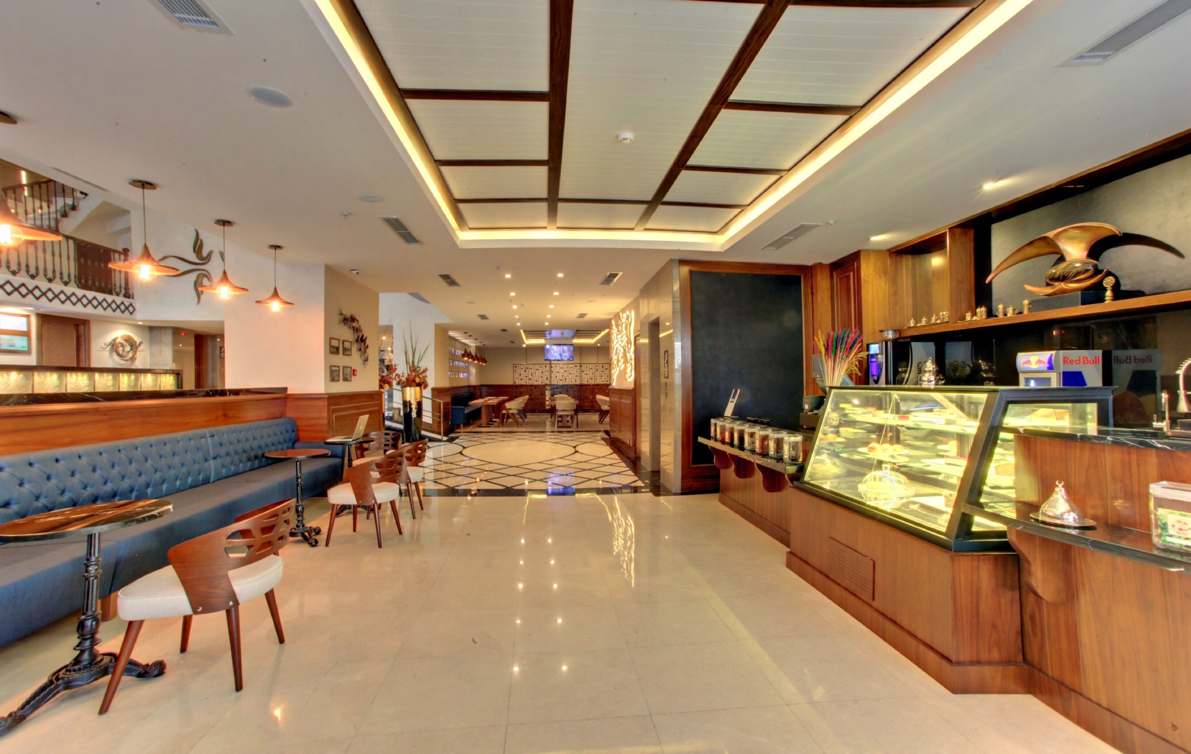 Un hall d’hôtel moderne comprenant un espace salon, un comptoir d’accueil et un présentoir de desserts.