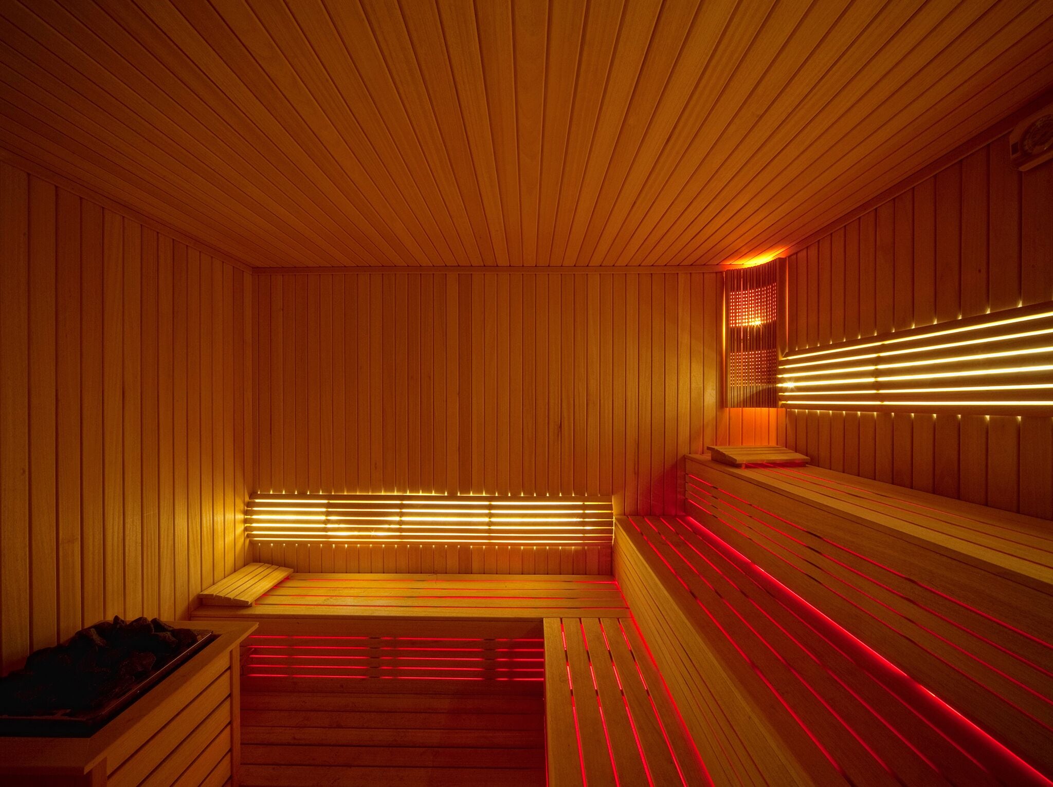 A sauna with wooden walls and benches, featuring red and yellow lighting.